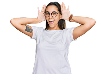 Obraz na płótnie Canvas Young hispanic woman wearing casual white t shirt smiling cheerful playing peek a boo with hands showing face. surprised and exited