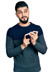 Young arab man with beard using glucose meter smiling looking to the side and staring away thinking.