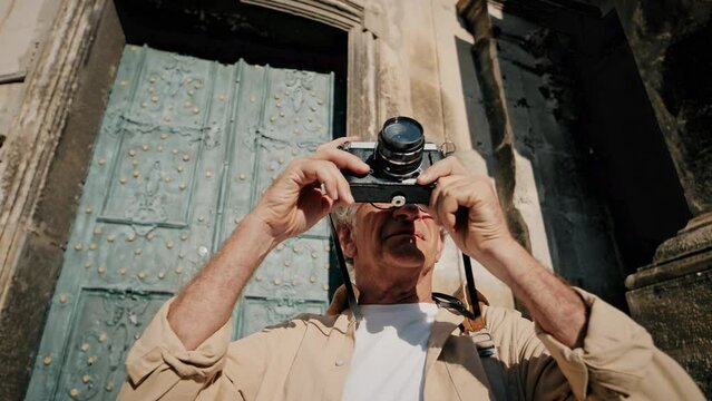 Camera sliding from side to side in front of older Caucasian male. Man standing and taking photos of wonderful architecture around him. Sunny day outside to explore. Tourism concept.