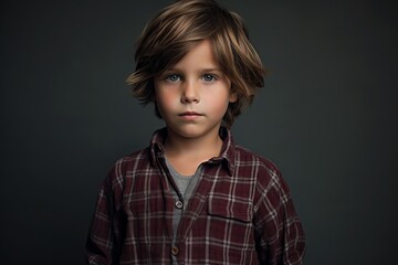 Portrait of a little boy in a plaid shirt on a dark background.