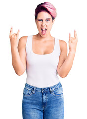 Young beautiful woman with pink hair wearing casual clothes shouting with crazy expression doing rock symbol with hands up. music star. heavy concept.