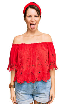 Young brunette woman with short hair wearing casual summer clothes and diadem sticking tongue out happy with funny expression. emotion concept.