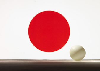 The pingpong ball stands on a surface in front of Japan flag.