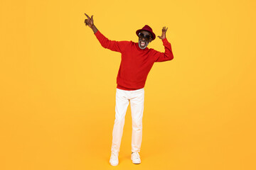 Joyful senior Black man in red sweater and stylish hat dancing and pointing upwards