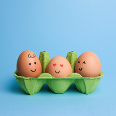 Cute easter eggs with funny faces in green box isolated on light blue background. Happy easter concept.