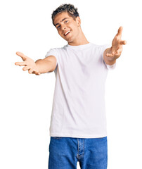 Fototapeta premium Young handsome man wearing casual white tshirt smiling cheerful offering hands giving assistance and acceptance.