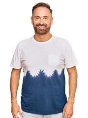 Handsome middle age man wearing casual tie dye tshirt with a happy and cool smile on face. lucky...