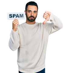 Young hispanic man with beard holding spam banner with angry face, negative sign showing dislike...