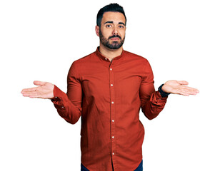 Young hispanic man with beard wearing casual shirt clueless and confused with open arms, no idea...