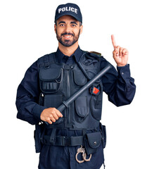 Young hispanic man wearing police uniform holding baton surprised with an idea or question pointing finger with happy face, number one