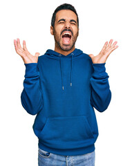 Young hispanic man wearing casual clothes celebrating mad and crazy for success with arms raised...