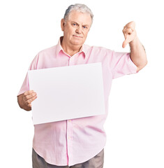 Senior grey-haired man holding blank empty banner with angry face, negative sign showing dislike with thumbs down, rejection concept