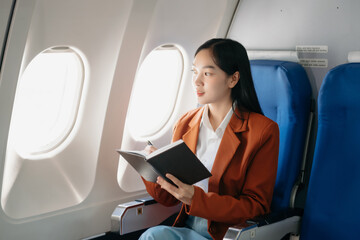 Attractive Asian female passenger of airplane sitting in comfortable seat while working laptop and tablet with mock up area using wireless connection.