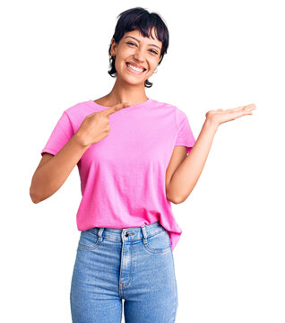 Young brunette woman with short hair wearing casual clothes amazed and smiling to the camera while presenting with hand and pointing with finger.