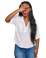 Young black woman wearing casual clothes peeking in shock covering face and eyes with hand, looking through fingers with embarrassed expression.