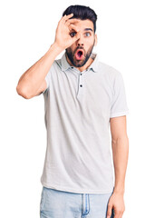 Fototapeta premium Young handsome man with beard wearing casual polo doing ok gesture shocked with surprised face, eye looking through fingers. unbelieving expression.