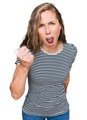 Young blonde woman wearing casual clothes angry and mad raising fist frustrated and furious while shouting with anger. rage and aggressive concept.