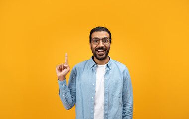 An excited man with a beard and glasses raises his index finger, sporting a bright smile
