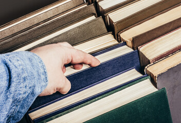 Photo of a male person is holding and choosing a book in their hand in library book stack.