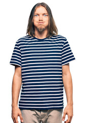 Handsome caucasian man with long hair wearing casual striped t-shirt puffing cheeks with funny face. mouth inflated with air, crazy expression.