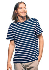 Handsome caucasian man with long hair wearing casual striped t-shirt looking away to side with smile on face, natural expression. laughing confident.