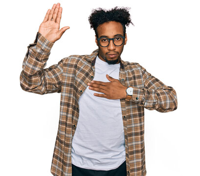 Young african american man with beard wearing casual clothes and glasses swearing with hand on chest and open palm, making a loyalty promise oath
