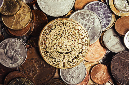 Photo of aztec or maya coin laying on a scattered pile of antique and old coins.