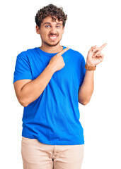 Young handsome man with curly hair wearing casual clothes pointing aside worried and nervous with...