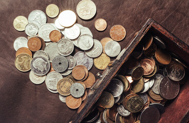 Photo of a wooden treasure box or chest filled with coins on table surface. Upper close up view.