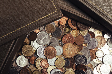 Photo of antique old books laying on scattered pile of world coins. Upper table view.