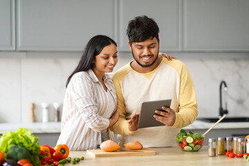 Beautiful loving spouses making food, watching video content on tablet