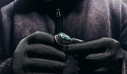 Photo of scary shaded hooded man silver ring with stone on dark background.