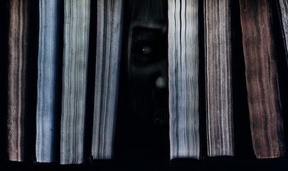 Photo of scary haunted ghost or monster face peeking out between books.