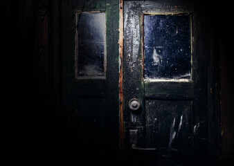 Photo of dusty, abandoned obsolete and shaded door with scary horror ghost face peaking out.