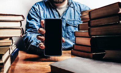 Photo of male person in denim shirt showing smartphone and sitting by the table with old book...