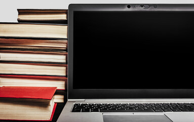 Photo of modern laptop or notebook laying on table with old antique books. Close up view.