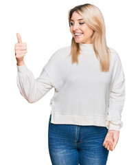 Young caucasian woman wearing casual winter sweater looking proud, smiling doing thumbs up gesture to the side