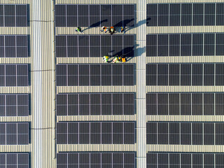 top aerial of engineer men inspects construction of solar cell panel or photovoltaic cell at roof top. Industrial Renewable energy of green power. factory at urban area. worker working on tower roof.