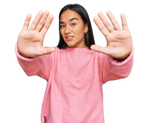 Young asian woman wearing casual winter sweater doing frame using hands palms and fingers, camera perspective