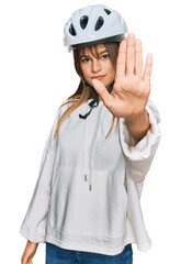 Teenager caucasian girl wearing bike helmet doing stop sing with palm of the hand. warning expression with negative and serious gesture on the face.