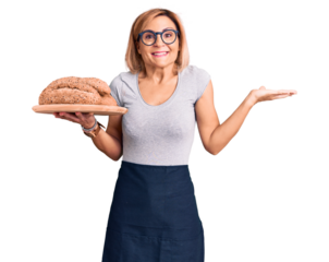 Young blonde woman holding wholemeal bread celebrating victory with happy smile and winner expression with raised hands
