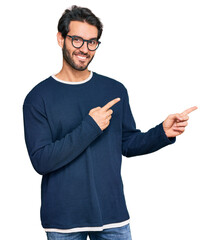 Young hispanic man wearing casual clothes and glasses smiling and looking at the camera pointing...