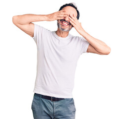 Fototapeta premium Middle age handsome man wearing casual t-shirt covering eyes with hands smiling cheerful and funny. blind concept.