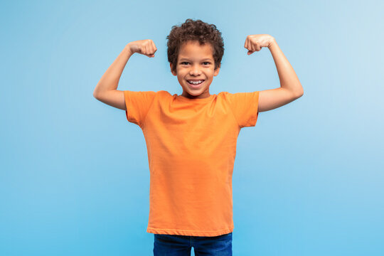 Strong, confident boy flexing muscles on blue background