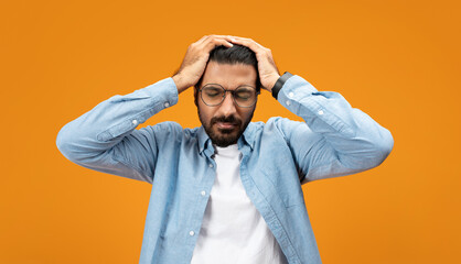 Stressed man in blue shirt holding head with both hands, eyes closed