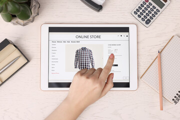 Woman with tablet shopping online at white wooden table, top view