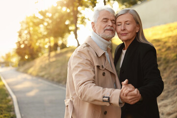 Affectionate senior couple dancing together outdoors, space for text