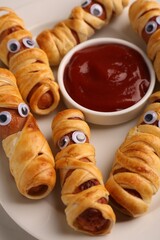 Plate with tasty sausage mummies for Halloween party and ketchup on table, closeup