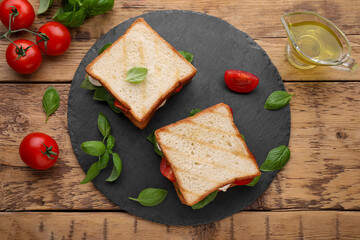 Fototapeta na wymiar Delicious Caprese sandwiches with mozzarella, tomatoes, basil and pesto sauce on wooden table, flat lay
