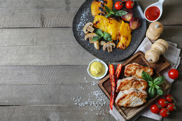 Delicious grilled meat and vegetables served with sauces on wooden table, flat lay. Space for text